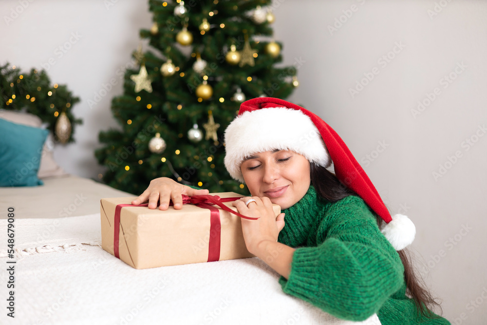 Merry Christmas. Portrait of a beautiful young woman in a cozy bedroom with a decorated Christmas tree in the background. Green sweater. Lifestyle Merry Christmas. Portrait of a beautiful young woman in a cozy bedroom with a decorated Christmas tree in the background. Green sweater. Lifestyle