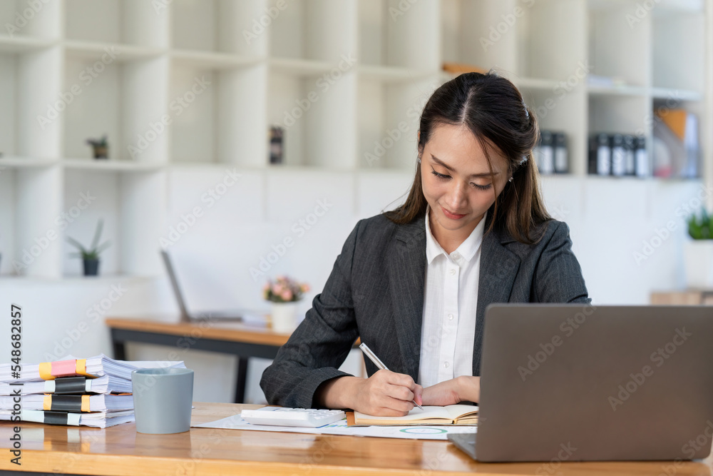 Asian accountant using calculator while taking notes on office desk. Asian accountant using calculator while taking notes on office desk.