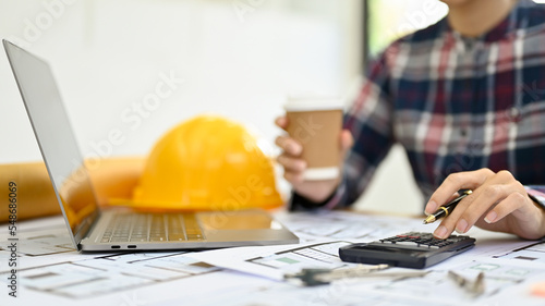 Male engineer or architect using scientific calculator, working at his desk while sipping coffee. photo