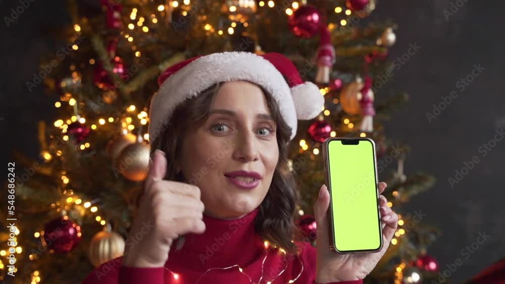 Woman in red sweater and Santa's hat holding a mobile phone with a green screen Woman in red sweater and Santa's hat holding a mobile phone with a green screen