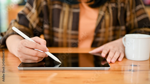An Asian female in flannel shirt using digital tablet to design her work while sitting in the cafe.