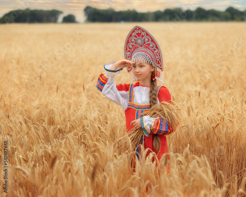 Littl girl kid in Russian national sarafan and a kokoshnik standing in a golden wheat field in summer day photo