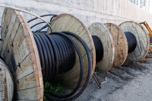 Large spool of black thick electrical wire or cable. Wooden reel with electrical industrial wires at a construction site. 