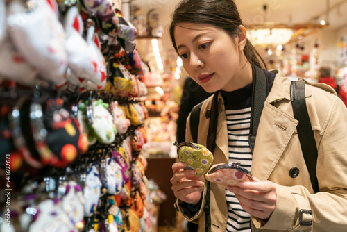 asian Japanese female consumer comparing two gamakuchi coin purses while deciding which to buy as souvenir in a shop on teramachi street at nishiki market in Kyoto japan