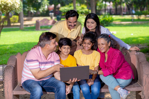 Happy indian or asian family using laptop at park