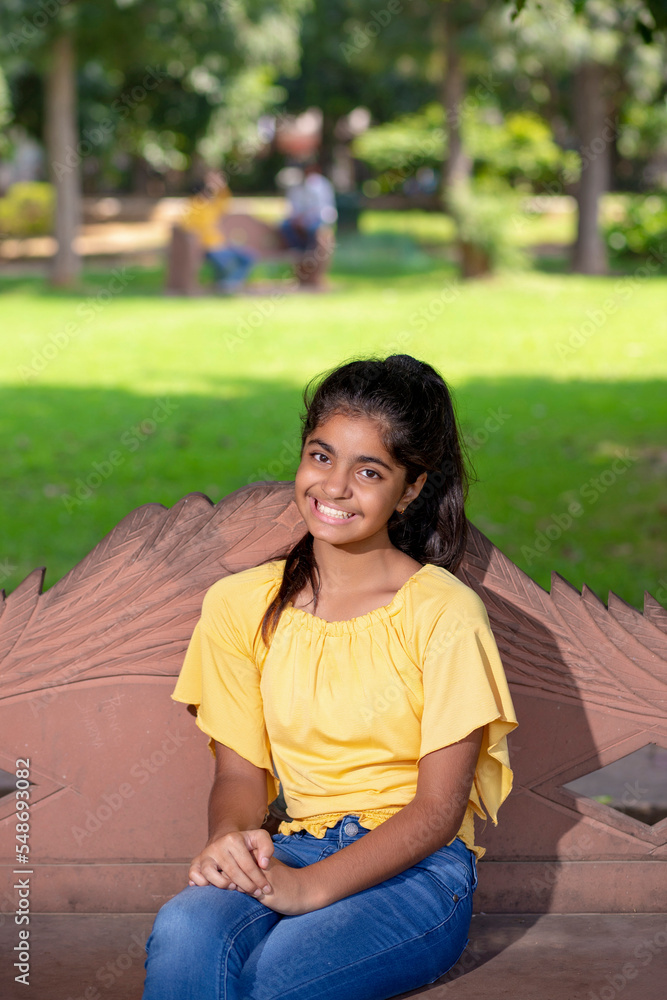 Naklejka premium Indian little girl sitting on bench at park