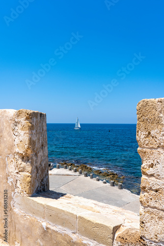 View through the battlements of the Firka Venetian Fortress on a sailing ship sailing on the sea of ​​Crete near Chania, Crete