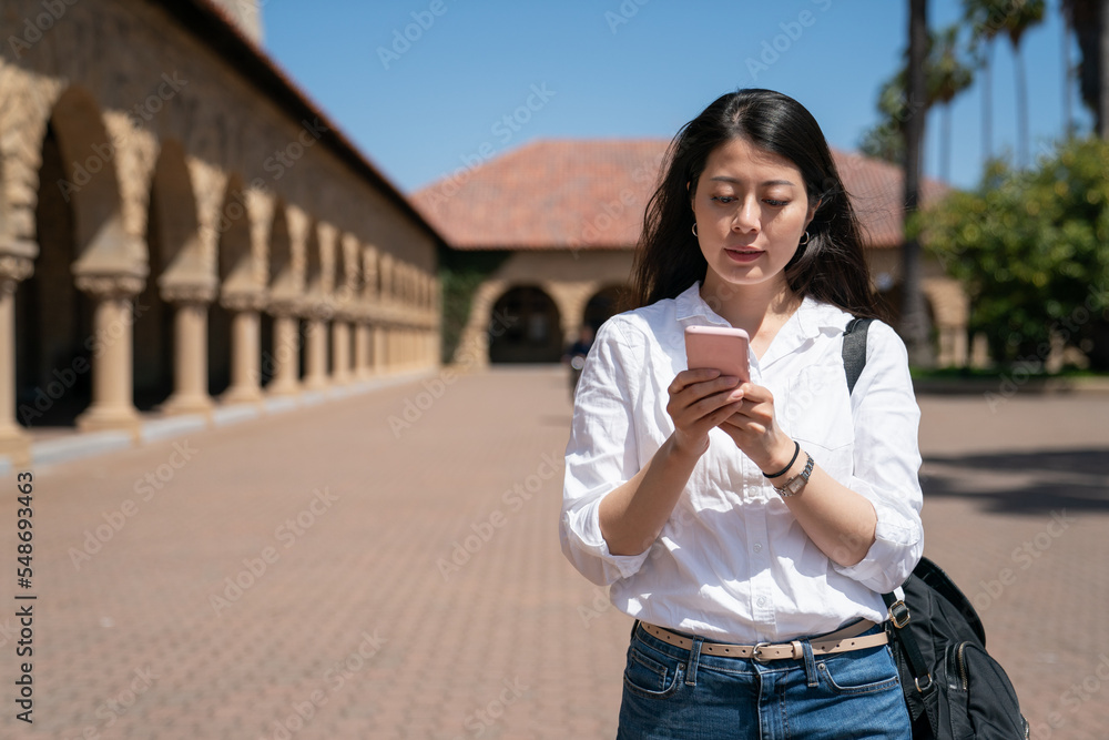 asian taiwanese woman international student reading course information on the phone near school Memorial Church on campus while sheâs on American study tour in California