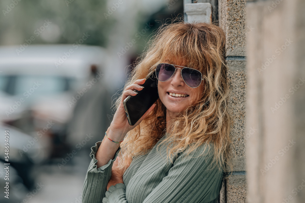 happy mature woman with smartphone on street wall