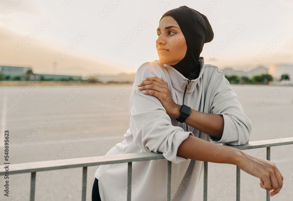 Athletic Muslim woman leaning on a fence outdoors Athletic Muslim woman leaning on a fence outdoors