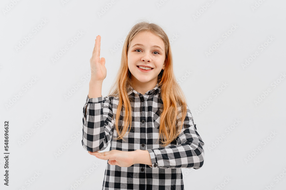 Fototapeta premium Beautiful teen girl with blonde hair wearing casual yellow t shirt, stands with his hand raised up over white studio background, smiling and gesturing hand. Education and school concept