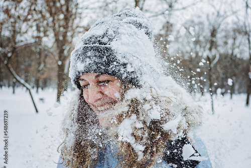 Close up outdoor winter portrait of woman in winter clothes. Candid portrait of young woman in winter time. Mom playing snowballs, walking under snow. Outdoors winter activities for adults, family.