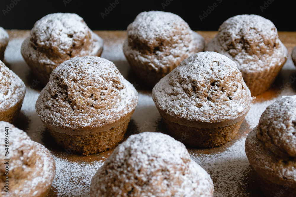 Close-up of delicious baked chocolate cupcakes on a wooden board and sprinkled with white powdered sugar Close-up of delicious baked chocolate cupcakes on a wooden board and sprinkled with white powdered sugar