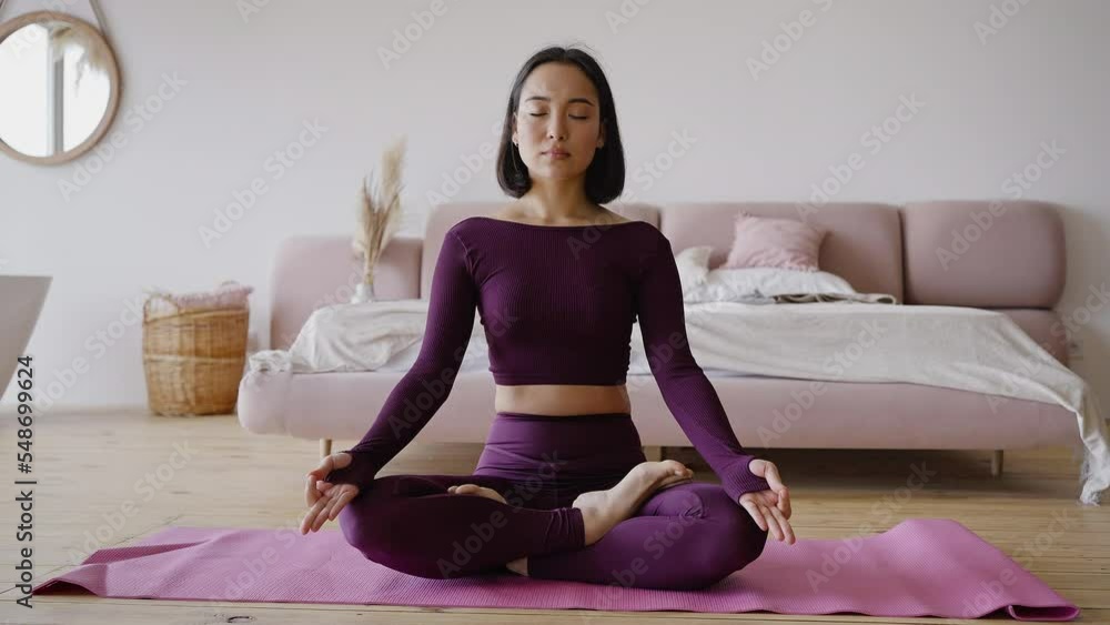 Young Asian woman meditates sitting in lotus pose in room Young Asian woman meditates sitting in lotus pose in room