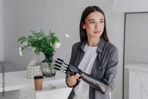 Purposeful brunette caucasian girl in grey shirt attaching artificial palm to her carbon mechanical hand looks aside  with wide opened mouth happy to have equal abilities after trauma.