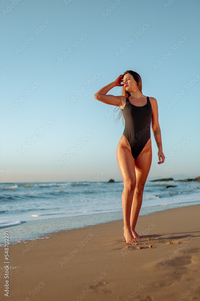 Jovem mulher de maiô preto no por do sol na praia