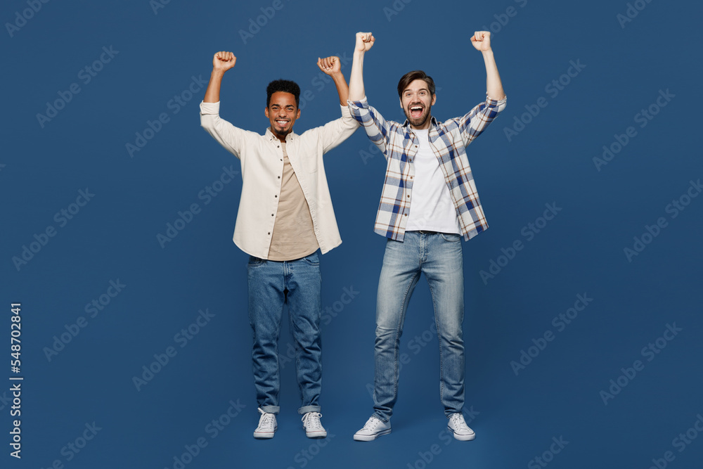 Obraz premium Full size young two friends men 20s wear white casual shirts together doing winner gesture celebrate clenching fists say yes isolated plain dark royal navy blue background. People lifestyle concept.