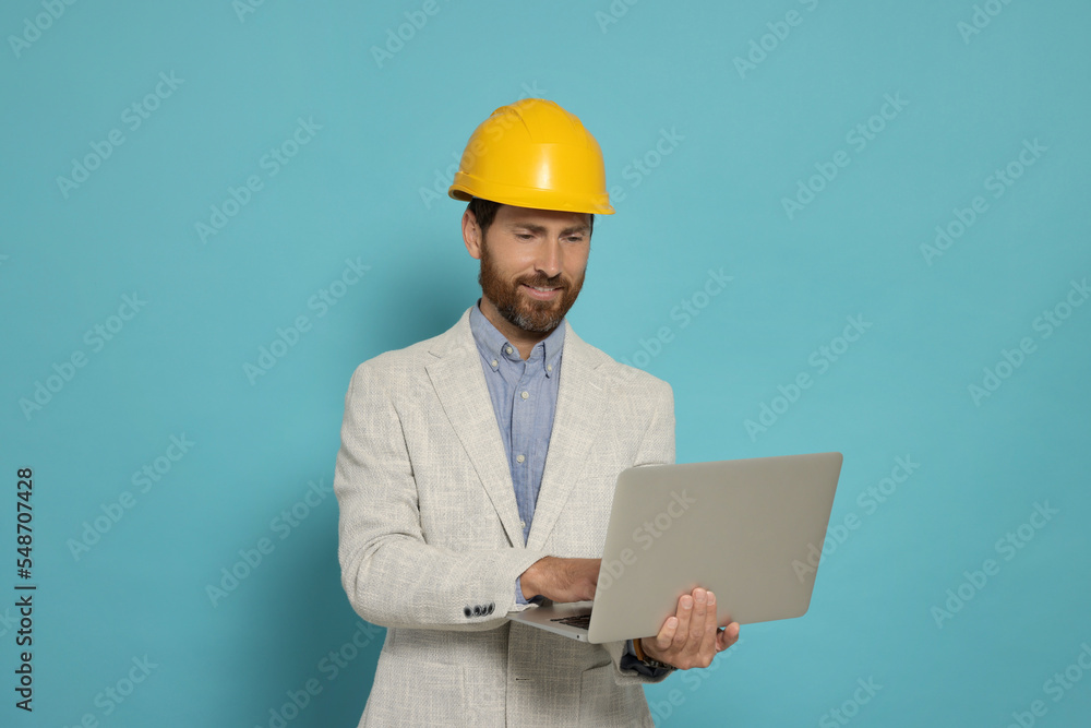 Professional engineer in hard hat with laptop on light blue background Professional engineer in hard hat with laptop on light blue background