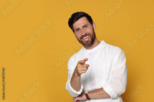 Smiling bearded man pointing forward finger on orange background. Space for text photo