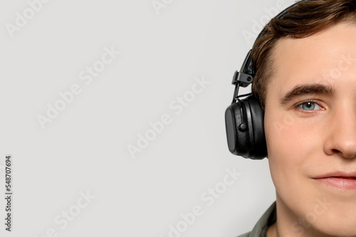 Handsome young man with headphones on light grey background, closeup. Space for text