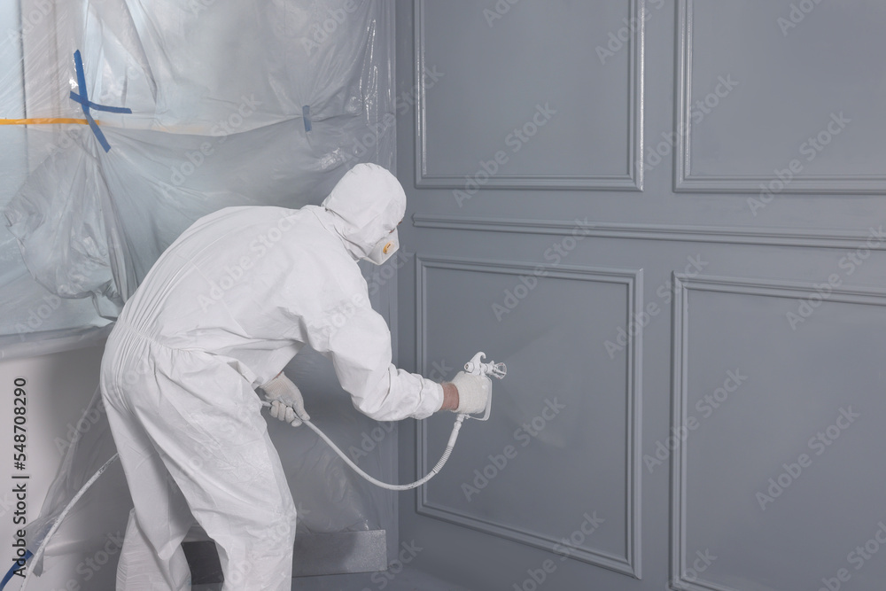 Decorator dyeing wall in grey color with spray paint, back view