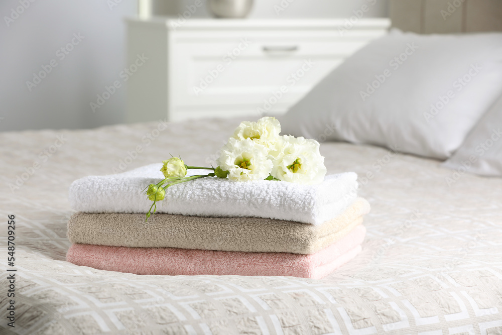 Terry towels with beautiful flowers on bed indoors, space for text Terry towels with beautiful flowers on bed indoors, space for text