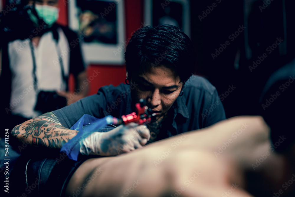 Professional tattooist makes the tattoo on a men waist, focusing on tattoo machines in a modern studio lowlight. Professional tattooist makes the tattoo on a men waist, focusing on tattoo machines in a modern studio lowlight.