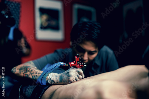 Professional tattooist makes the tattoo on a men waist, focusing on tattoo machines in a modern studio lowlight.