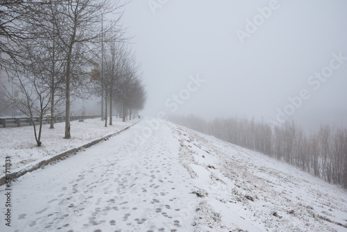 Frosty foggy morning in winter on the sidewalk and footprints in the snow.