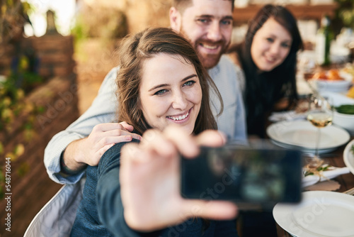 Friends, selfie and dinner with party and celebration, woman holding smartphone for photo and Christmas or Thanksgiving dinner party. Happy, celebrate and food, having meal together and smile.