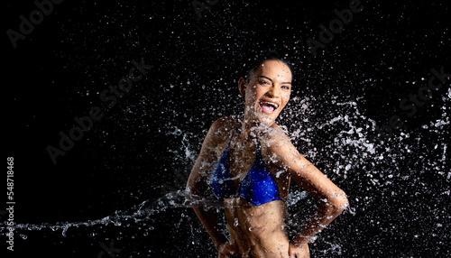 Tanned skin Asian woman in bikini poses in aqua studio. Splash Drops of water spread to body. Fun emotion female girl on water attack fluttering and stop motion freeze shot  black background isolated