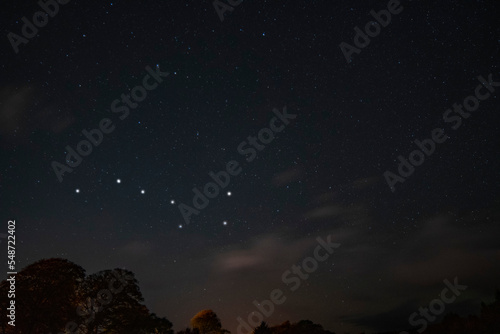A night full of stars and some clouds and trees in the background. The Plough highlighted Night view of the sky many constellations. The Big Dipper