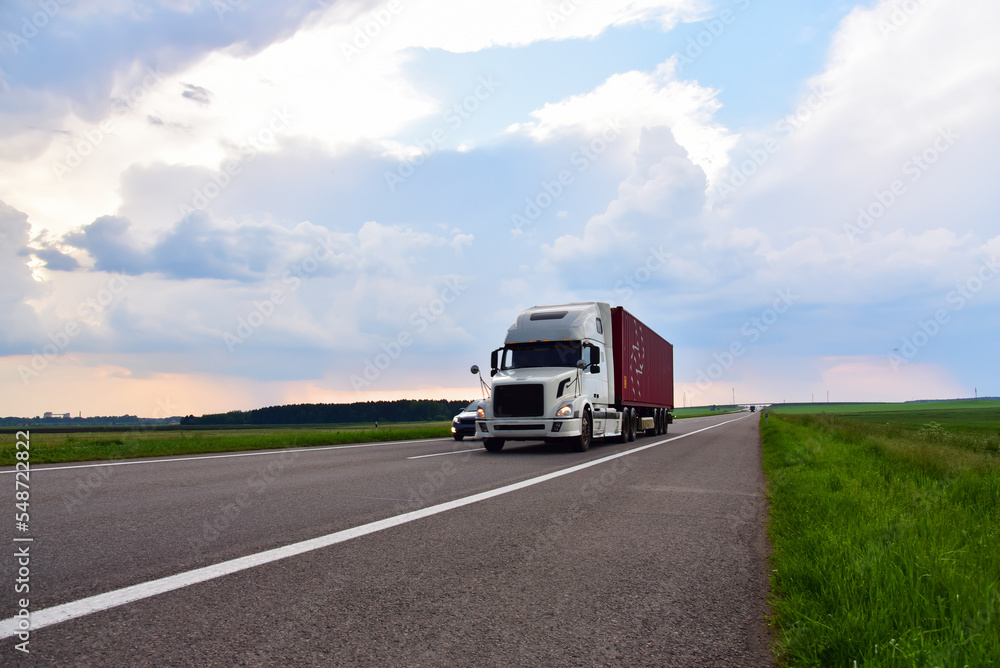 American semi truck transporting sea container on highway on sunset. Shipping Containers Delivery, Maritime Services and Transport logistics. Shipping, Import - Export. Object in motion, soft focus. American semi truck transporting sea container on highway on sunset. Shipping Containers Delivery, Maritime Services and Transport logistics. Shipping, Import - Export. Object in motion, soft focus.