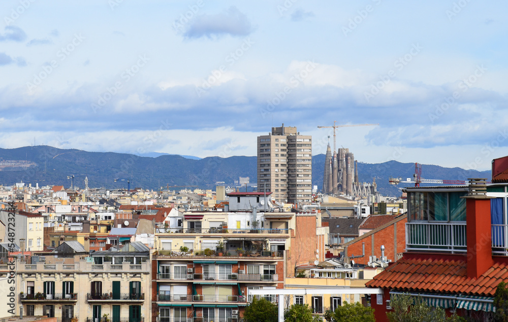 Naklejka premium Roofs of buildings. Barcelona Spain, high angle view city skyline. Mountains skyline. Rooftop view in Barcelona. Facade of old residential building at hills and mountain. Historic building in rock.