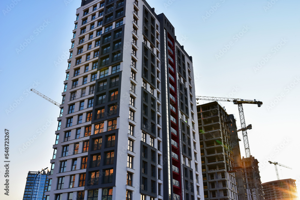 Facade of a new residential building with windows in flats. Construction of a residential multi-storey house with apartments. Tower crane on construction in built environment. Buildings renovation.