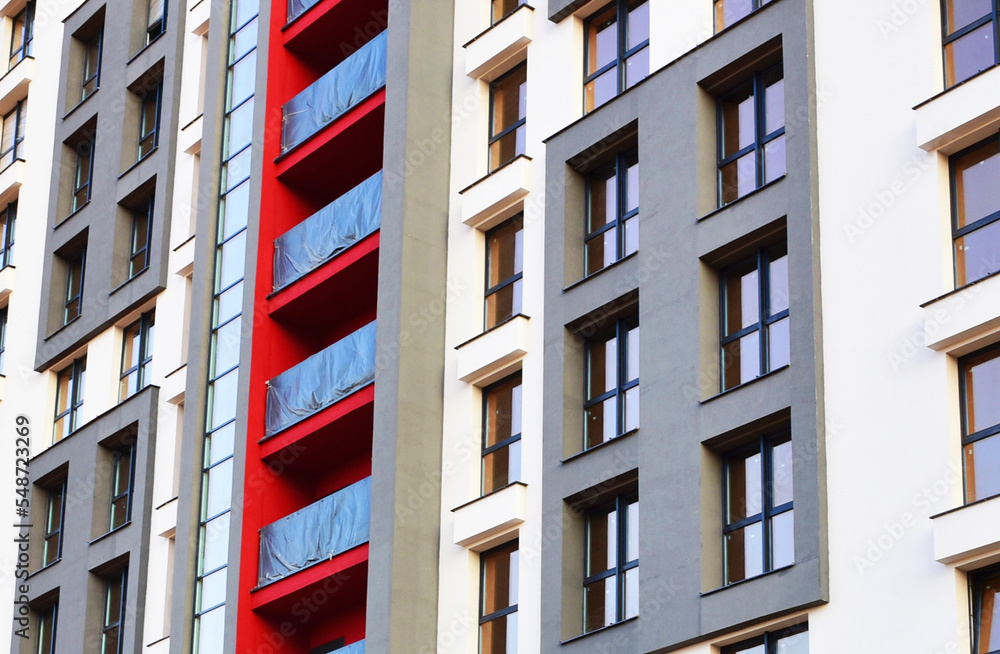 Fototapeta premium Facade of a new residential building with windows in flats. Construction of the skyscraper. Tall house renovation project. Painting facade of building during construction of housing under renovation