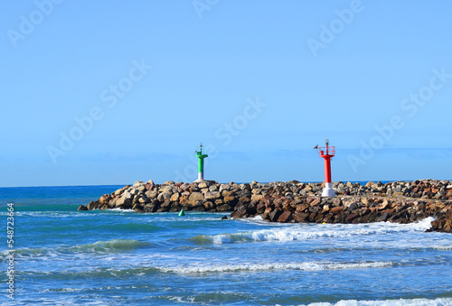 Lighthouse on Wave breaker and Stone pier at sea. View of the mediterranean sea with the Lighthouses at rocky shore. Wave breakers along the shoreline with Lighthouse at ocean. Lighthouse on blue sky.