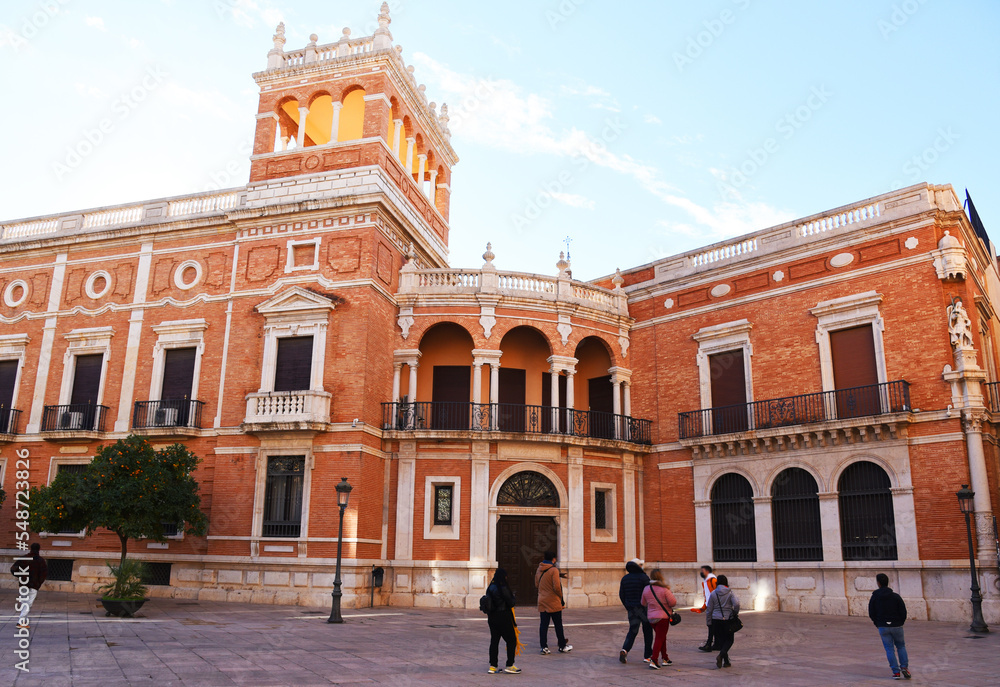 Archiepiscopal Palace of Valencia. Palace in the Old Town known as Cabildo de Valencia. Orange trees with Green leaves at facade building. Urban landscape. Ancient Architecture, Brick House.