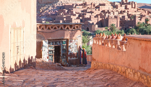 A traditionally dressed hawker selling souvenirs opens a shop at the morning - Panoramic View on Ait Ben Haddou near Ouarzazate river, Atlas Mountains, Morocco, North Africa 