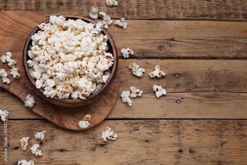 Bowl of tasty popcorn on wooden table, above view. Space for text