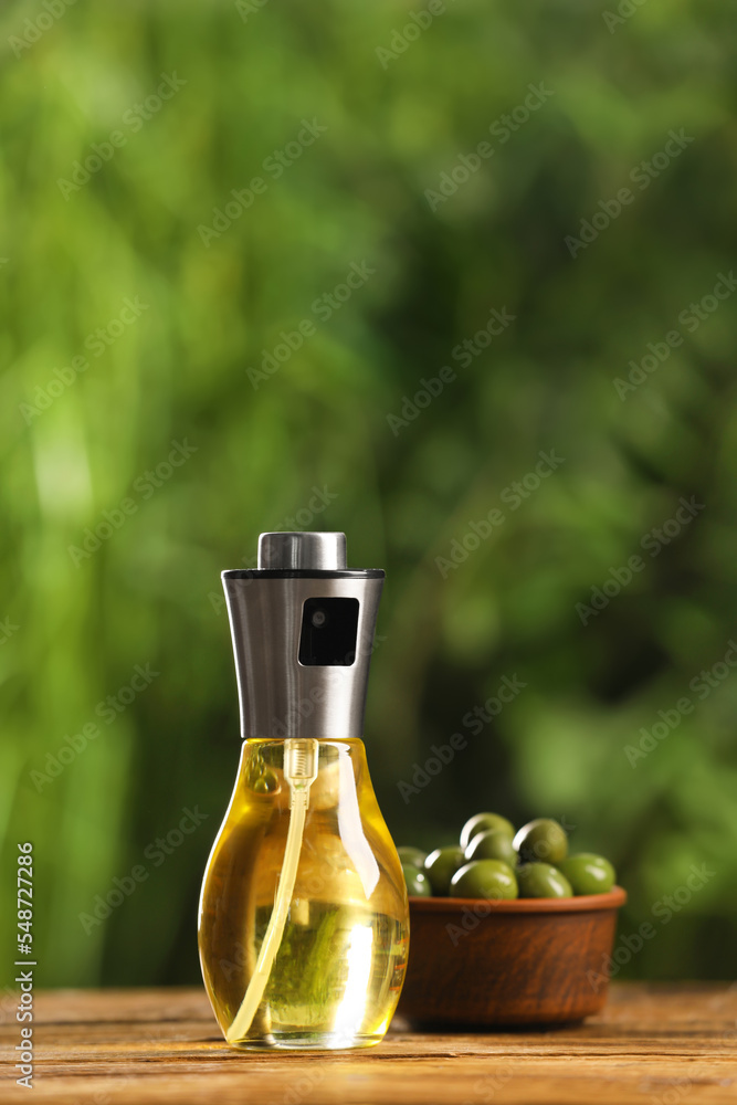 Spray bottle with cooking oil and olives on wooden table against blurred background Spray bottle with cooking oil and olives on wooden table against blurred background