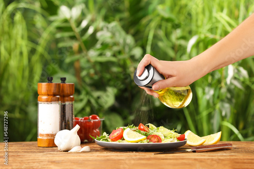 Fototapeta Woman dressing delicious salad with cooking oil at wooden table against blurred