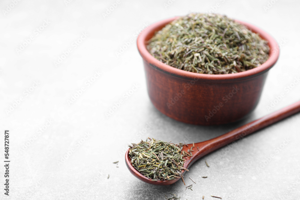 Fototapeta premium Bowl and spoon with dried thyme on grey table, closeup. Space for text