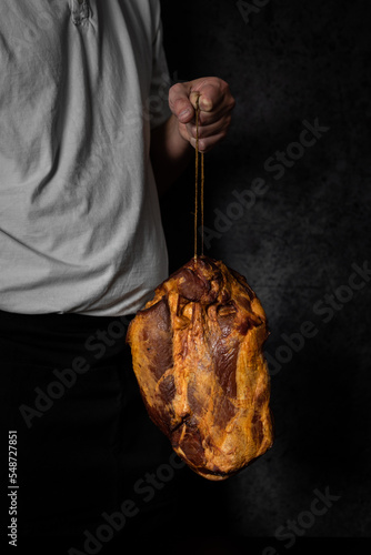 A man holds a whole smoked dried meat in his hand on a rope on a dark background. Minimalistic food concept.