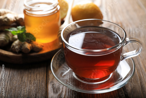 Cup of delicious ginger tea and ingredients on wooden table, closeup