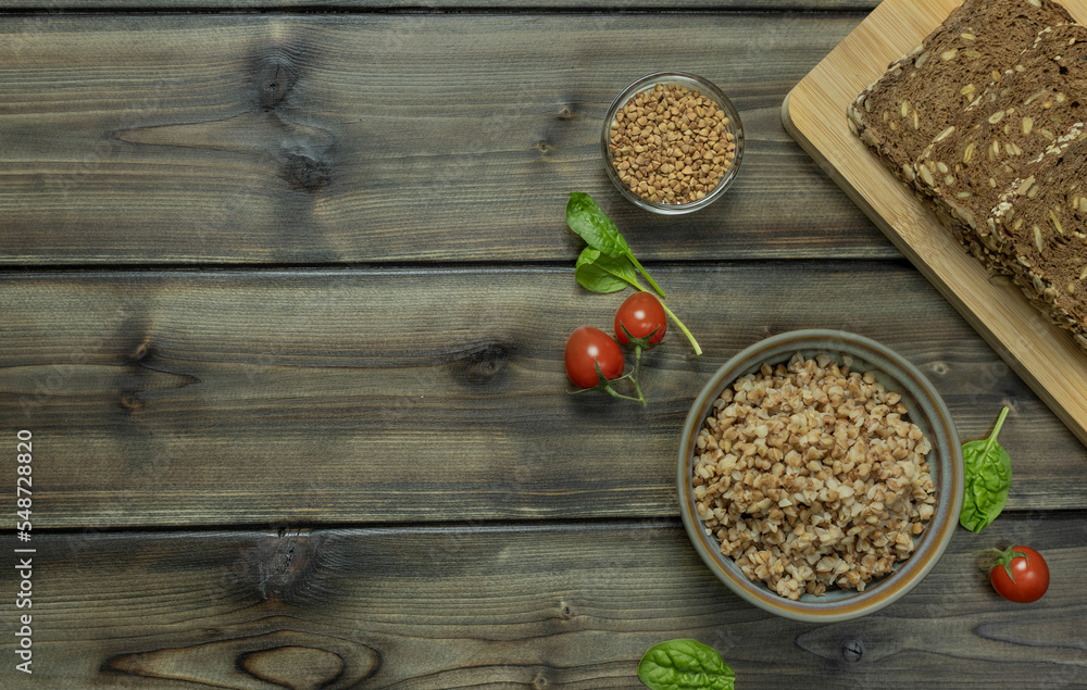 buckwheat porridge in a plate with rye bread, lettuce leaves and cherry tomatoes on a dark wooden background. buckwheat porridge in a plate with rye bread, lettuce leaves and cherry tomatoes on a dark wooden background.