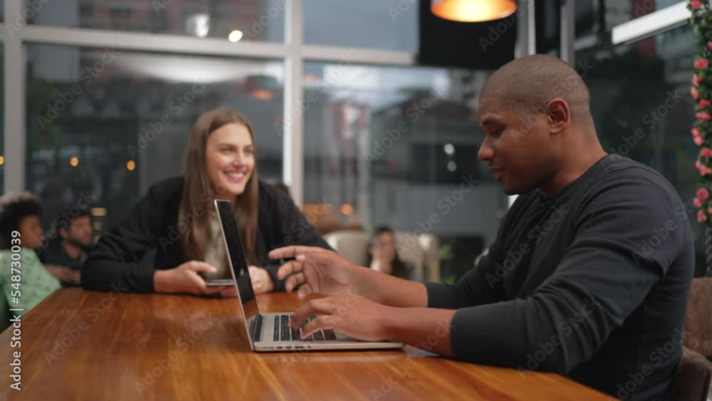 People inside coffee shop at night. African American man using laptop talking with female friend inside cafe restaurant place People inside coffee shop at night. African American man using laptop talking with female friend inside cafe restaurant place