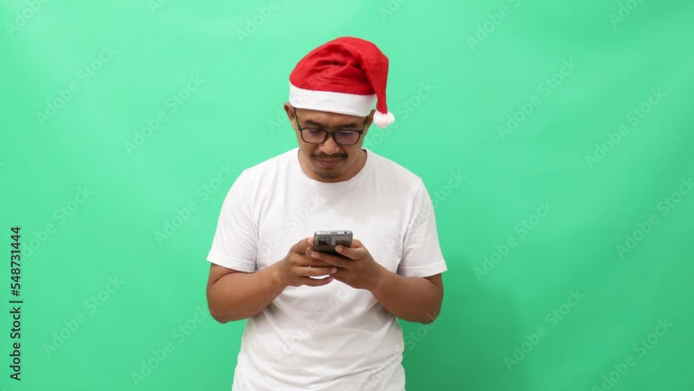 Surprised asian man standing while holding cell phone. Christmas concept isolated on green background Surprised asian man standing while holding cell phone. Christmas concept isolated on green background