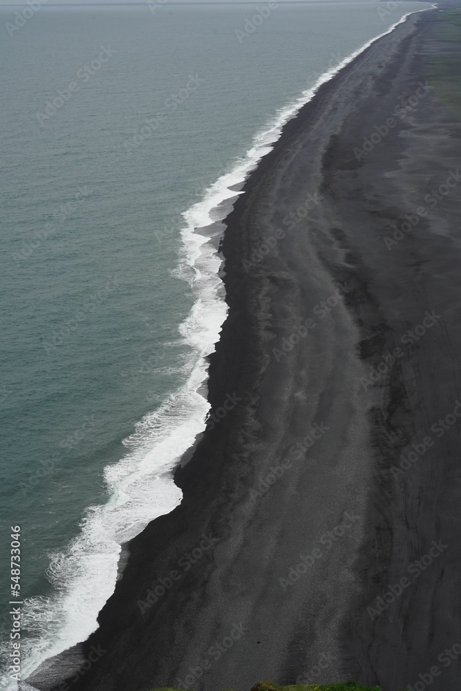 Naklejka premium Ocean with white foamy waves splashing into the black beach