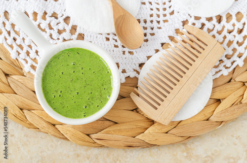 Homemade matcha green tea (kelp, algae, spirulina) face or hair mask (scrub) in a small white bowl and wooden hairbrush. Natural beauty treatment and spa recipe. Top view.